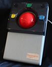 Gray and black rectangular device with a red trackball and yellow, green, blue buttons